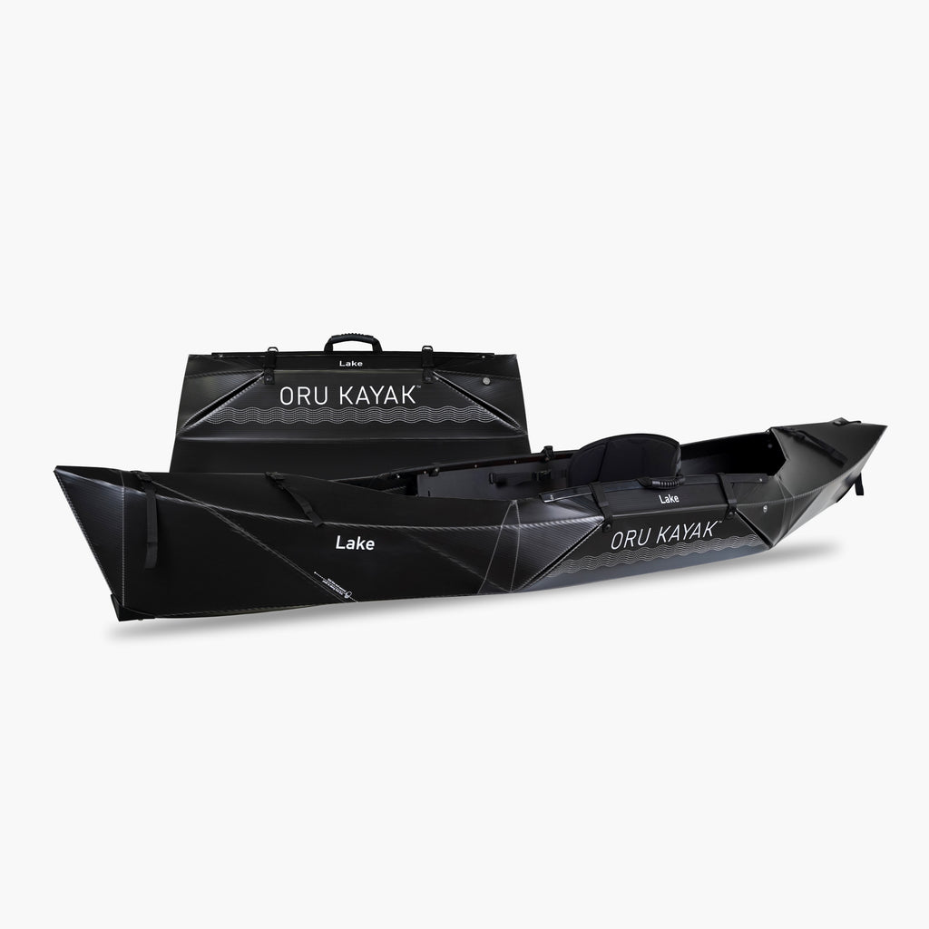 Side view of the Oru Kayak Lake model in black, shown fully assembled in front of its compact folded box form.